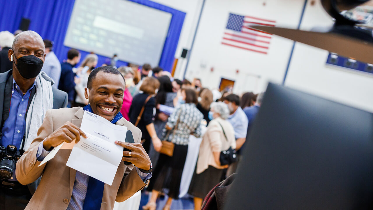 A medical student smiles broadly and points to his residency match letter