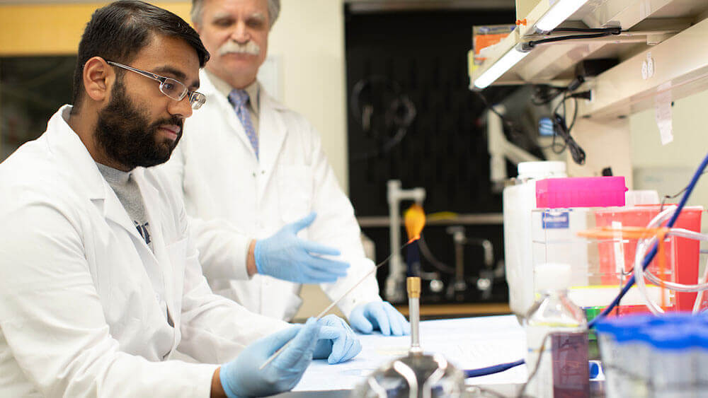 A medical student wearing a lab coat and gloves uses a flame in the research lab