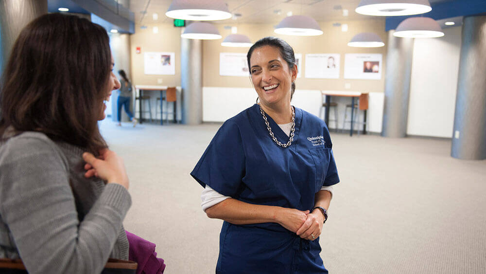 Professor Traci Marquis-Eydman wearing navy blue scrubs talks with a student in a school hallway