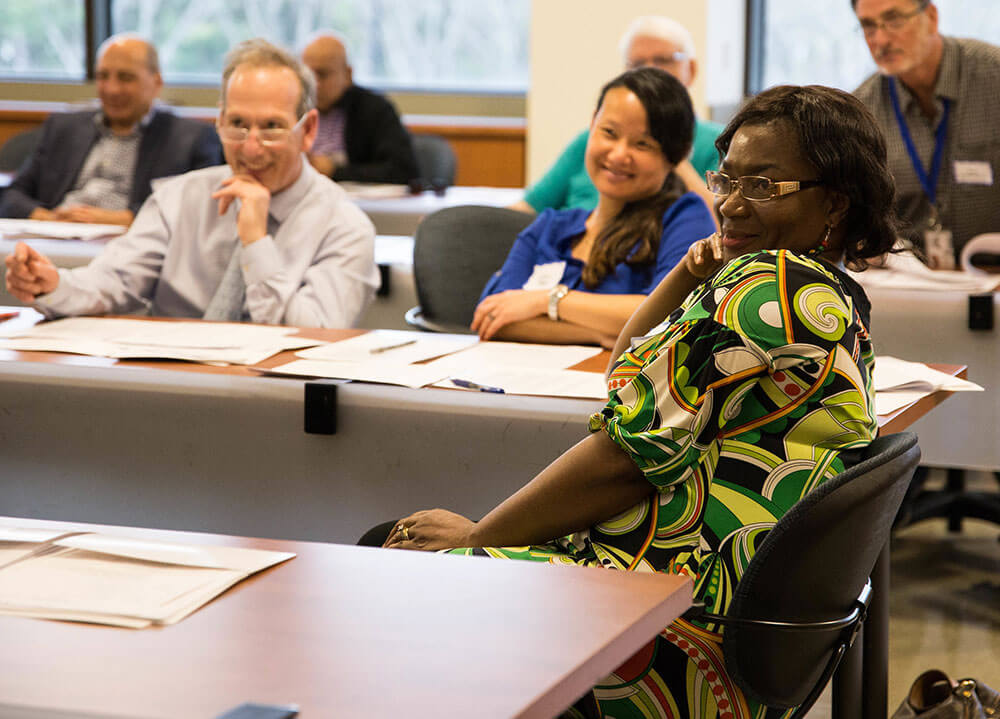 A group of faculty mentors of area hospitals sit and smile while attending a workshop in a classroom